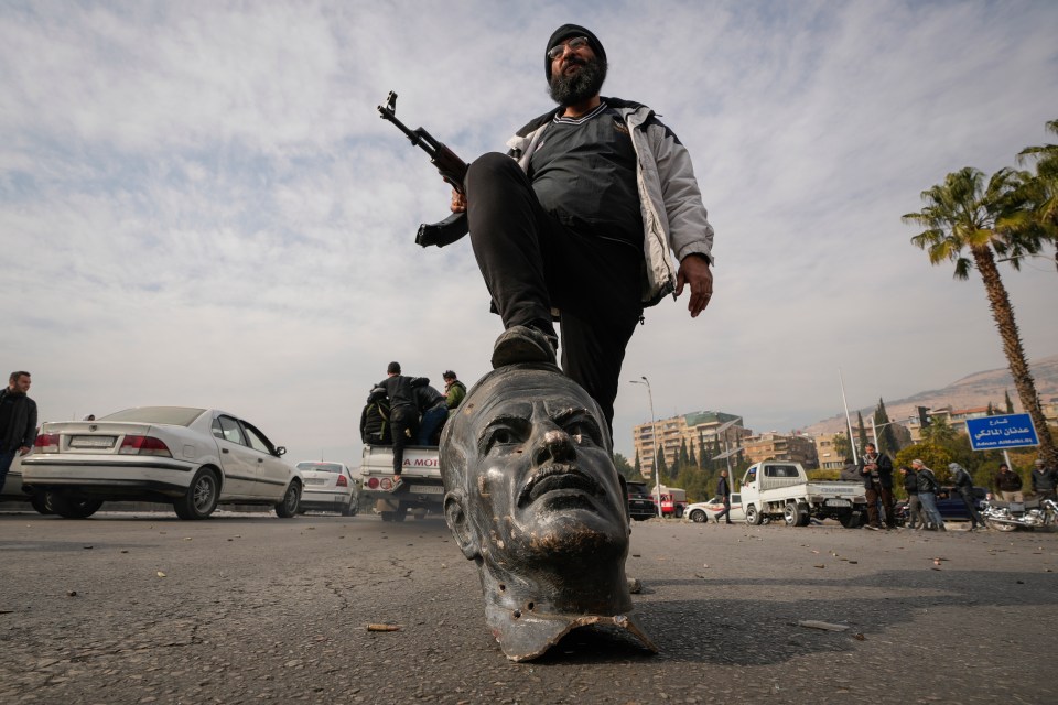 An opposition fighter steps on a broken bust of the late Syrian President Hafez Assad