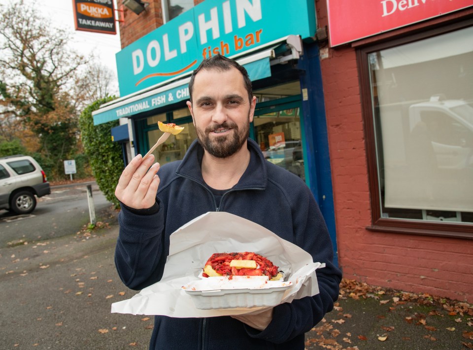 Man holding fish and chips outside a fish bar.