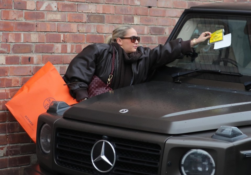 Woman placing parking ticket on Mercedes G-Wagon.