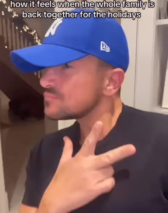 Man wearing a blue baseball cap making a gesture expressing holiday family togetherness.