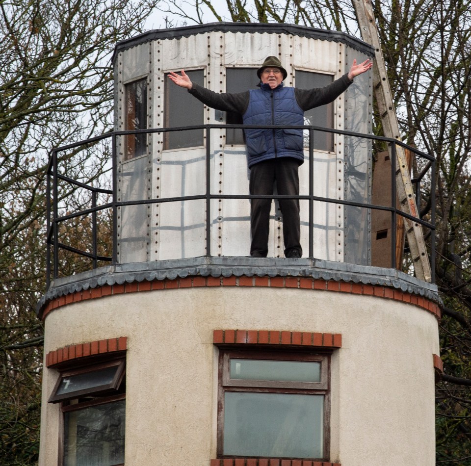 Man standing on top of a small lighthouse-like structure he built.