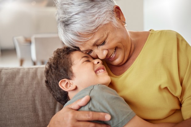 A grandmother and grandson hug on a couch.