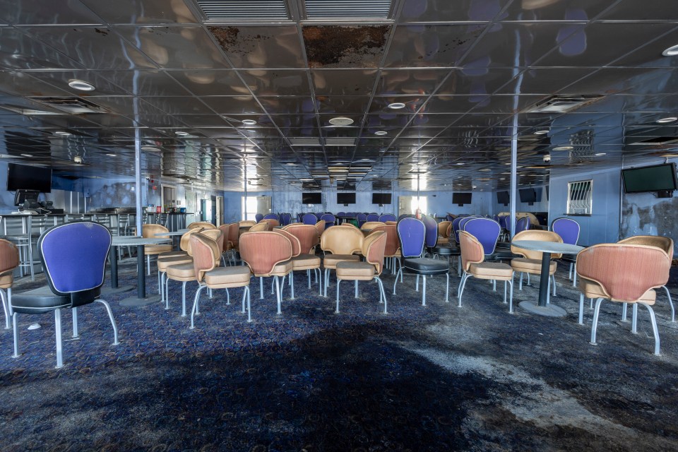 Interior of an abandoned casino boat with chairs and tables.