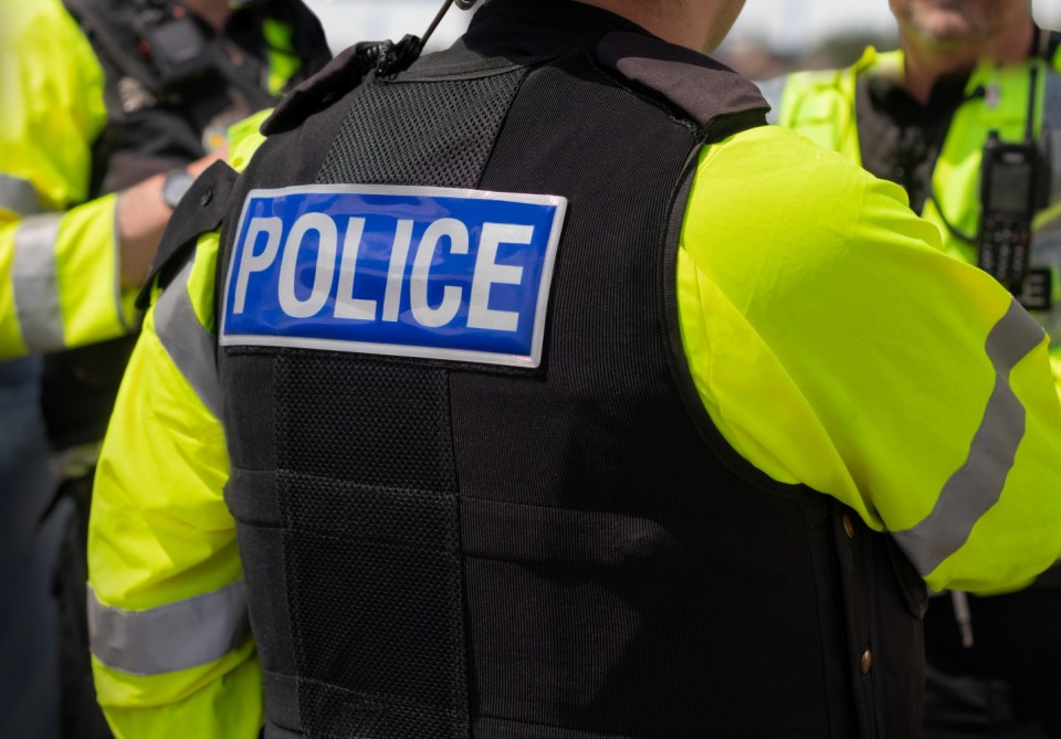 Close-up of 'POLICE' marking written on the back of a hi-visibility stab proof vest worn by a trio of police officers at the scene of an incident. Officers enforce the law, establish public order and protect citizens.