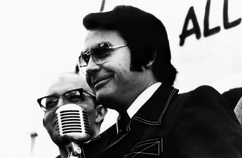 Black and white portrait of Jim Jones at a microphone.