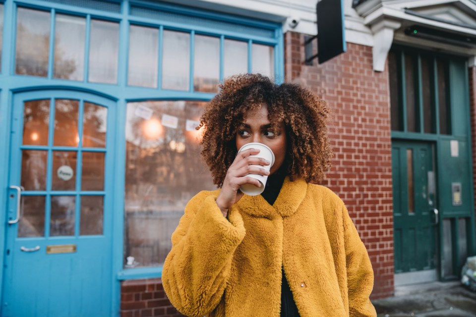 Young woman with afro hair drinks coffee outdoors.