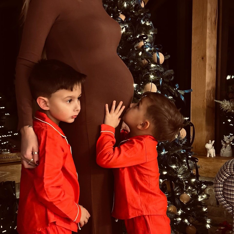 Pregnant woman with two young sons in red pajamas near a Christmas tree.