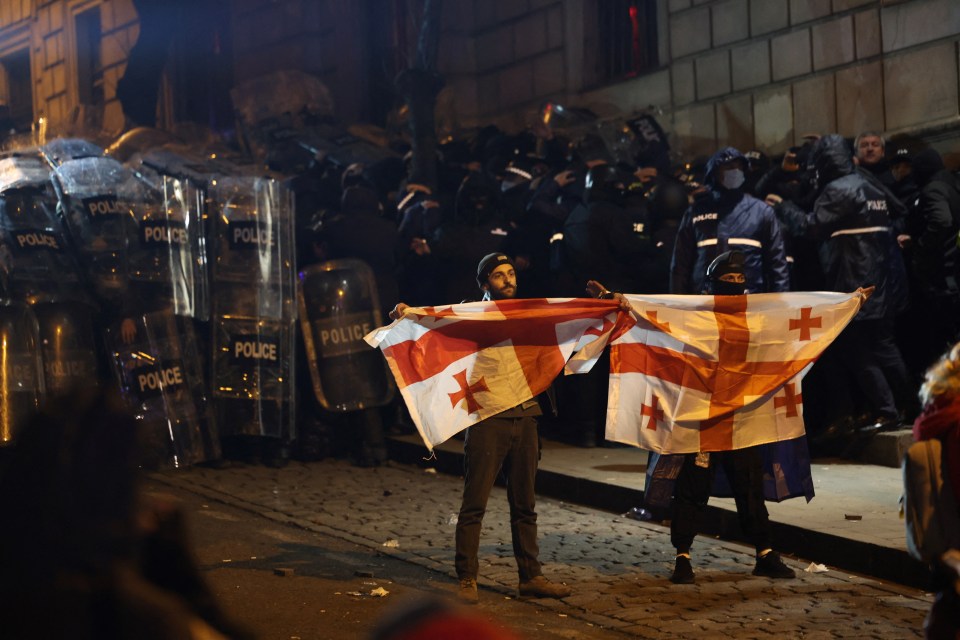 Protesters hold Georgian national flags in front of riot police