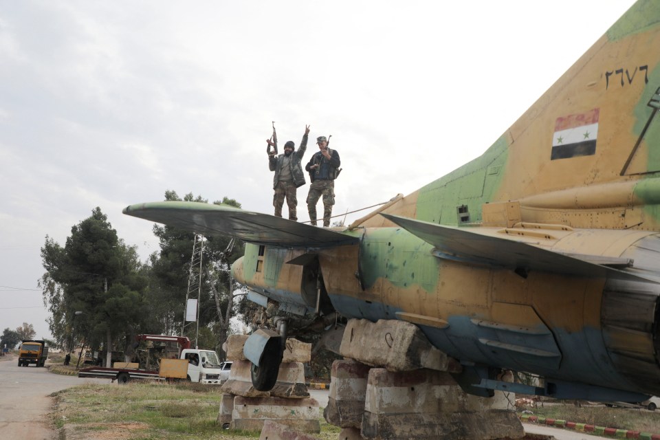 A rebel fighter gestures the victory sign while standing on a military aircraft that belonged to forces loyal to Bashar al-Assad government, inside Hama’s military airport