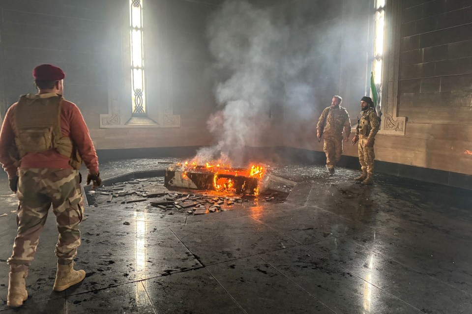 Rebel fighters stand next to the burning gravesite of Syria’s late president Hafez al-Assad