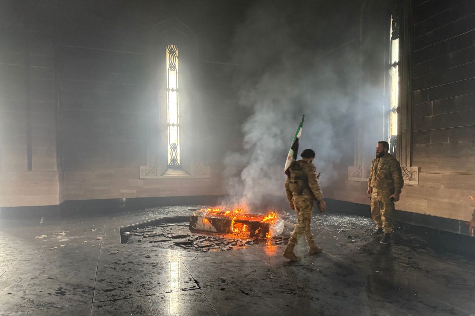 Rebel fighters stand next to the burning grave of Hafez