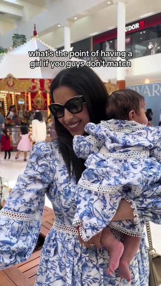 Woman in a blue floral dress holding a baby in a matching dress in a mall.