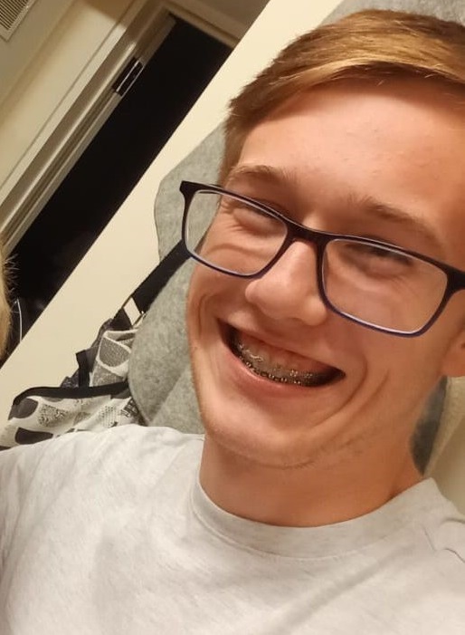 Close-up selfie of a smiling young man wearing glasses and braces.