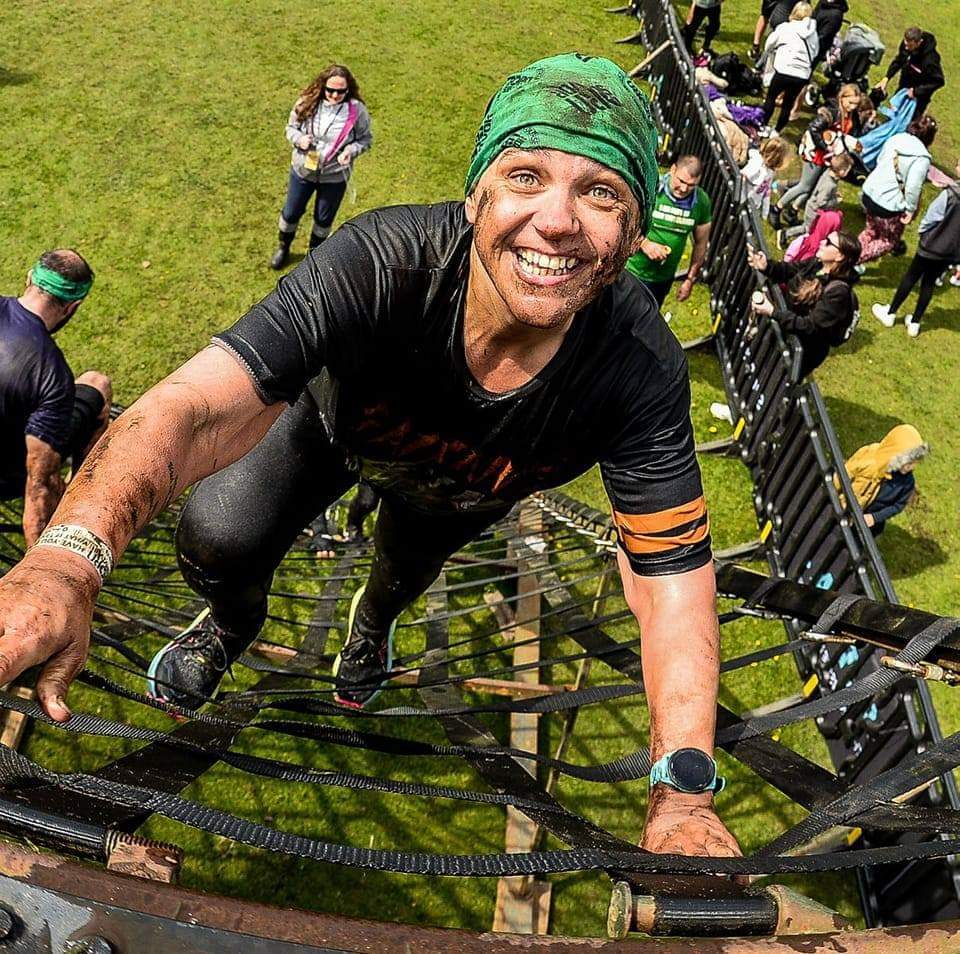 Muddy man climbing a cargo net during an obstacle course.