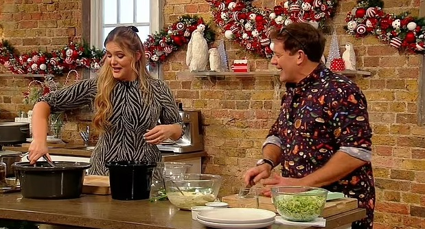 Poppy O'Toole and a male chef cooking together in a festive kitchen.