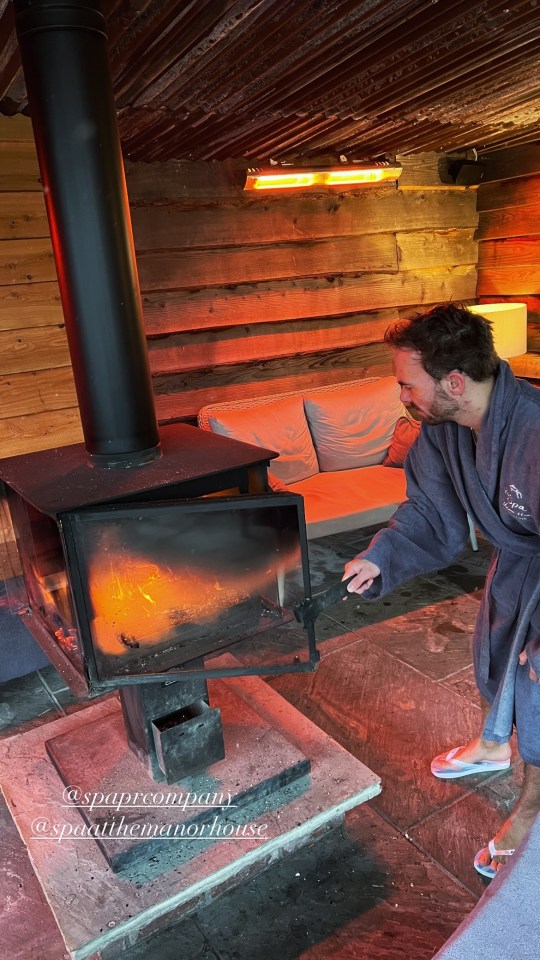 Man in robe tending a fire in a wood-burning stove.