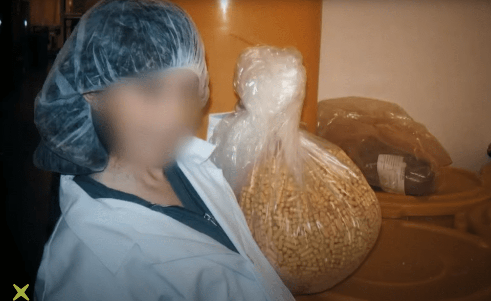 A person in a lab coat and hairnet holds a large bag of pills.