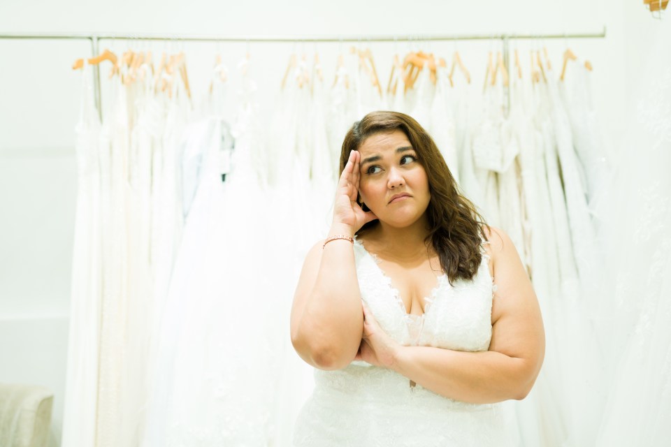 Plus-size bride looking stressed while trying on a wedding dress.