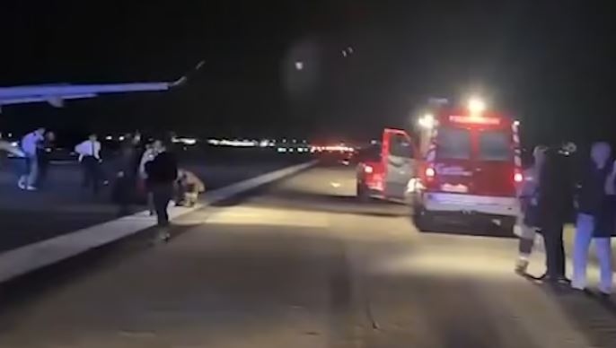 Passengers evacuating a Swiss Airlines plane on a runway at night, with emergency vehicles present.