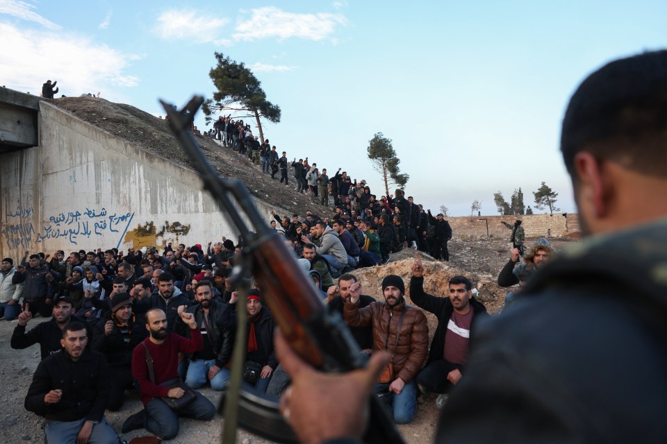 A rebel fighter stands over captured government troops