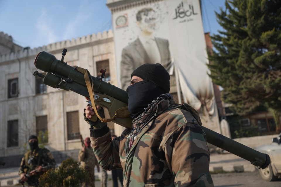 A fighter stands in front of an image of Bashar al-Assad riddled with bullets