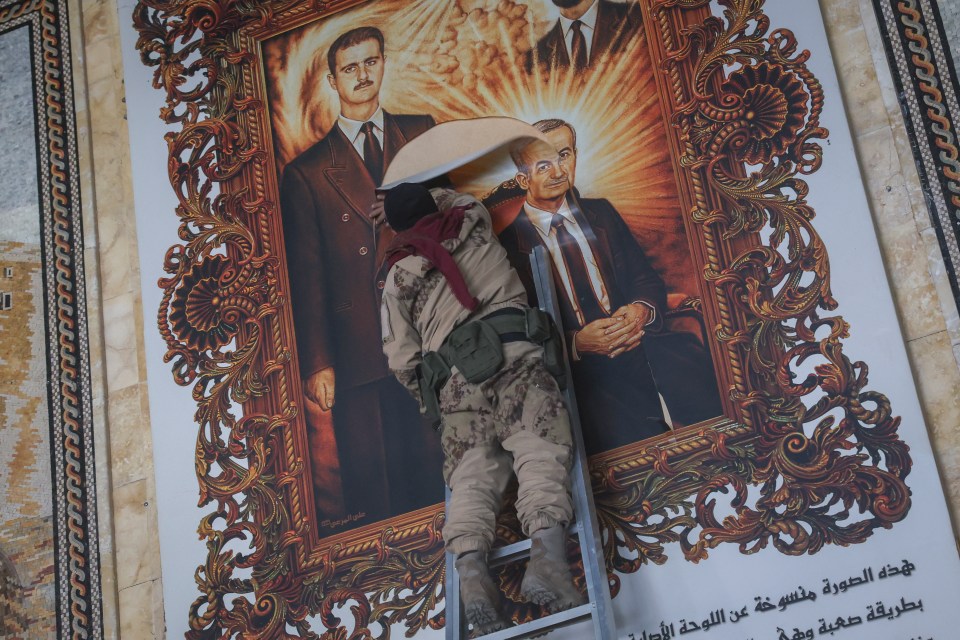 A Syrian opposition fighter tears up a painting depicting Assad and his late father Hazef Assad