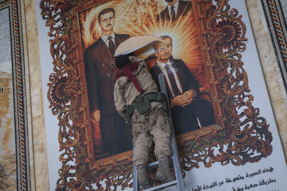 A Syrian opposition fighter tears a painting depicting the Assads