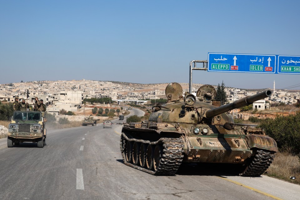 Syrian opposition fighters drive by an abandoned tank