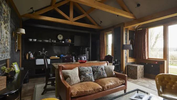 Interior of a UK hotel room in a national park, featuring a leather sofa, a kitchenette, and large windows with views of the outdoors.