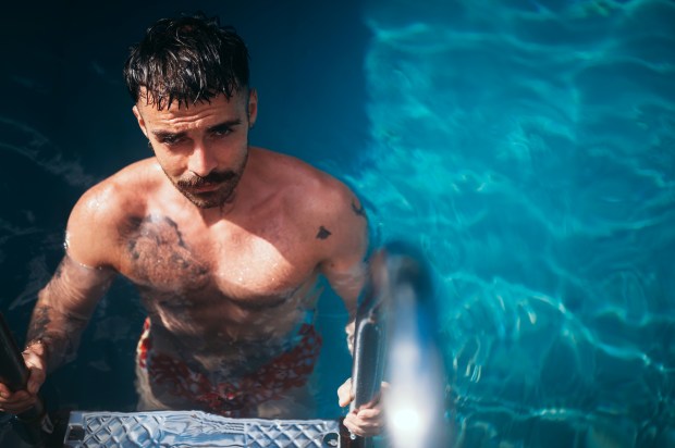 A young man with tattoos emerges from a swimming pool.