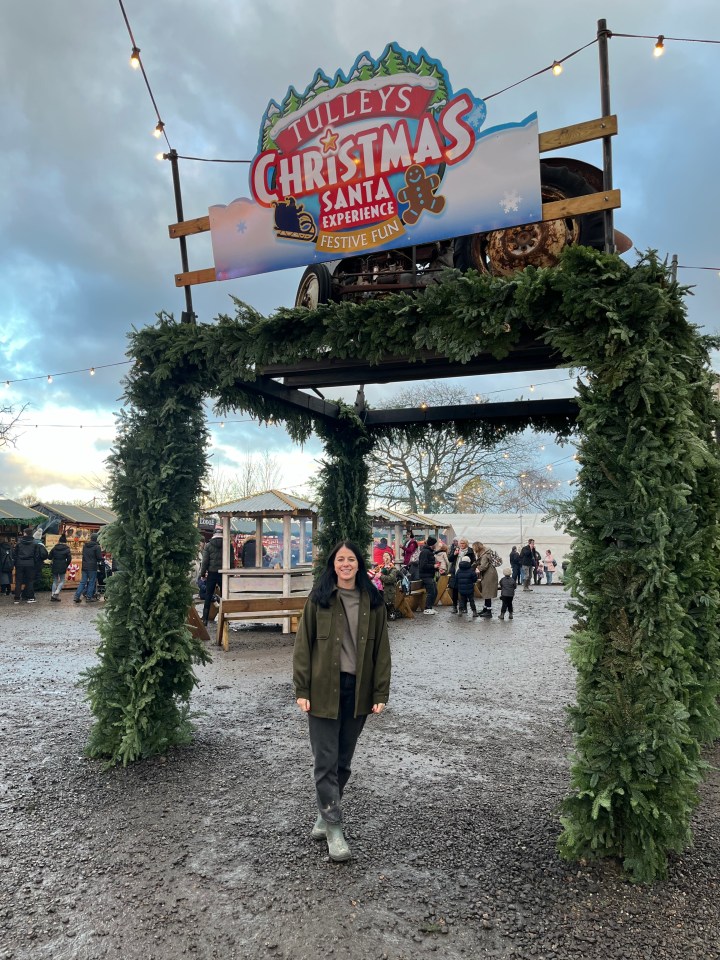 Woman standing under Tulley's Christmas Santa Experience sign at a Christmas market.