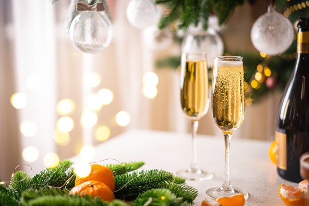 Two glasses of champagne and tangerines on a table in front of a decorated Christmas tree.