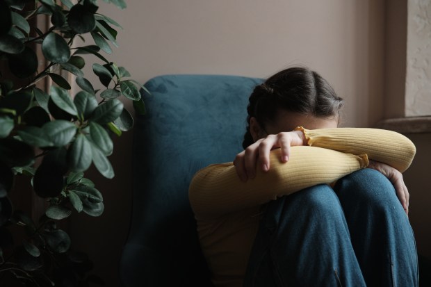 A teenager sits alone, covering their face with their arms, appearing upset.