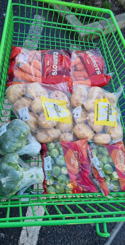 Shopping cart filled with carrots, potatoes, broccoli, and Brussels sprouts.