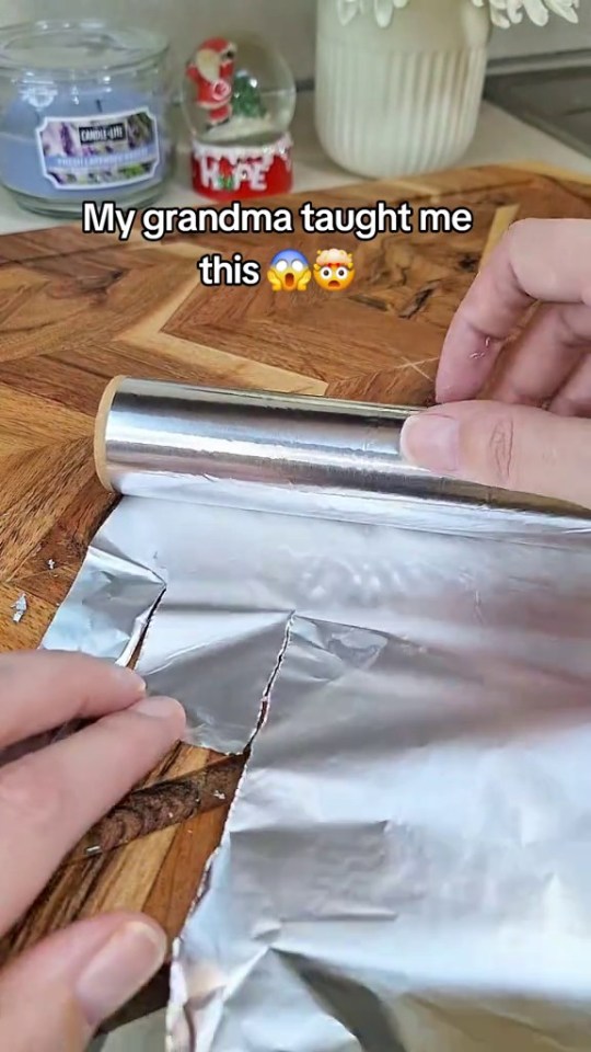 Hands demonstrating a method for easily unrolling crumpled aluminum foil.