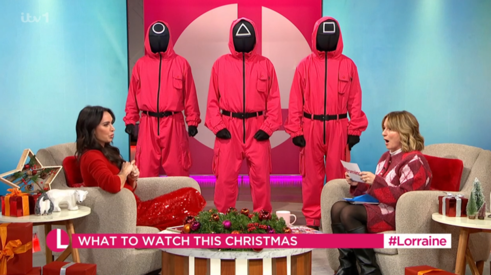 Christine Lampard and a guest on the Lorraine show react to three people in Squid Game costumes.