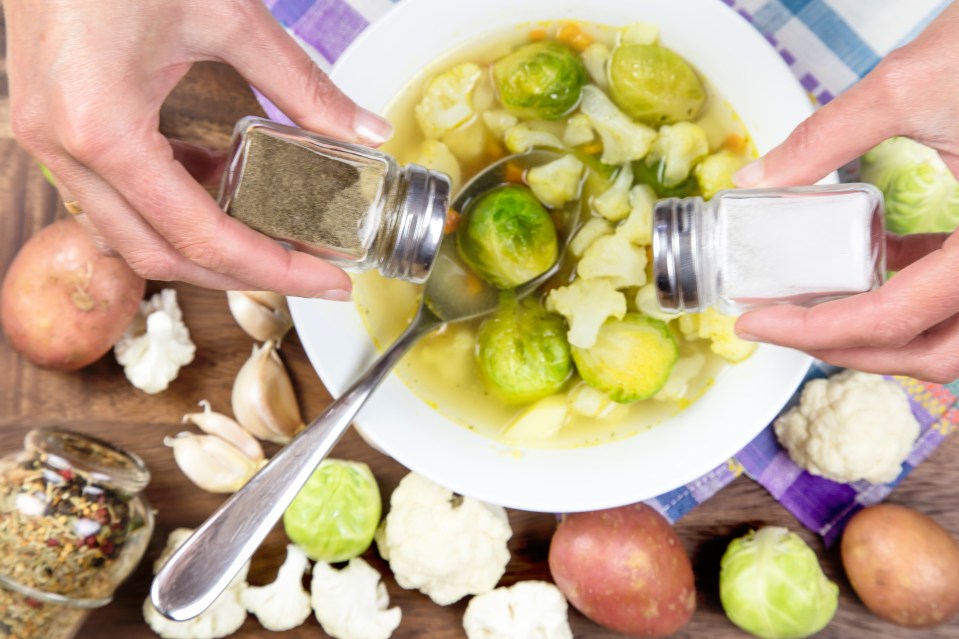 Hands seasoning vegetable soup with salt and pepper.