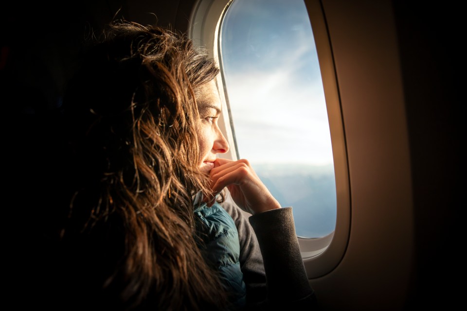 Woman looking out airplane window at sunrise.