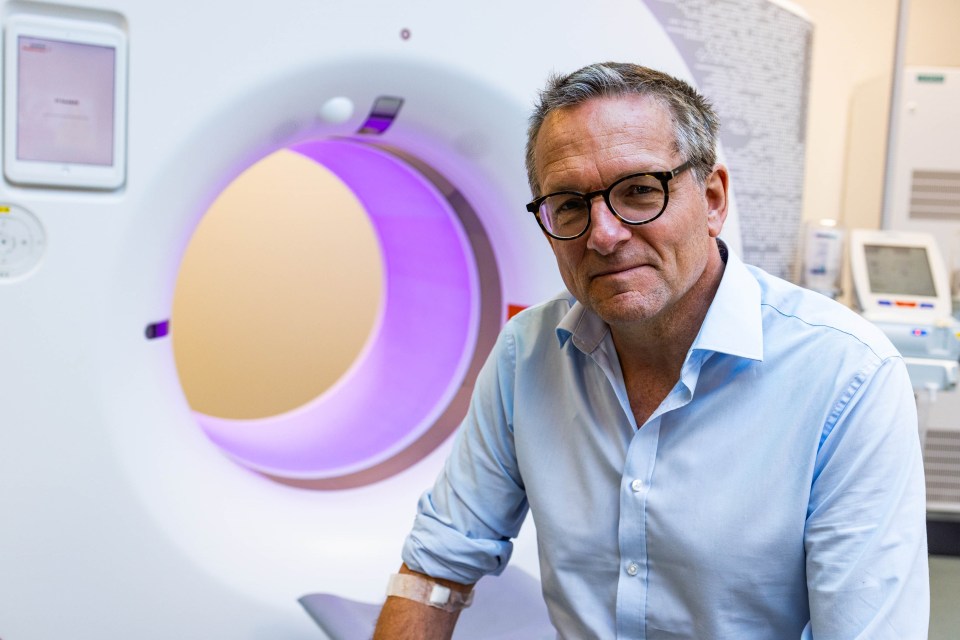 Man in light blue shirt sitting in front of a CT scanner.