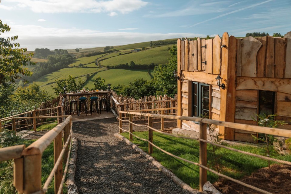 Wooden cabin with outdoor seating area overlooking a green valley.