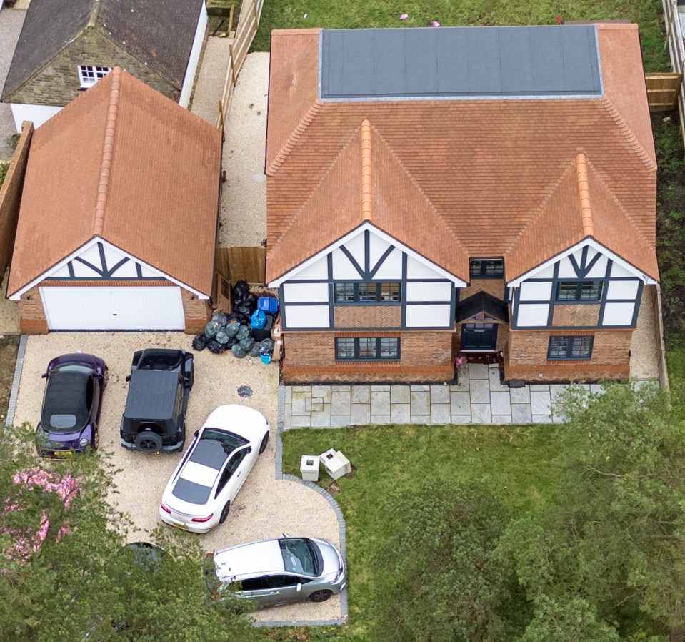 Aerial view of a new house with several cars parked in the driveway and garbage bags on the ground.