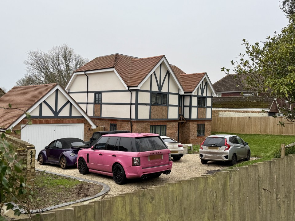 Photo of a new house with several cars parked in the driveway, including a pink Range Rover.