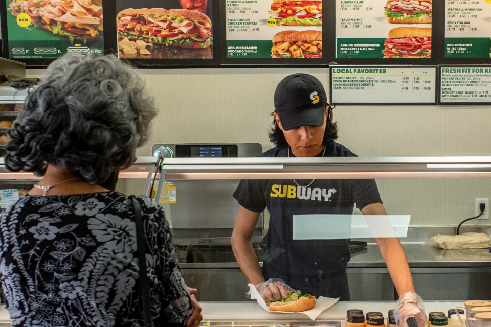 A Subway employee prepares a sandwich for a customer.