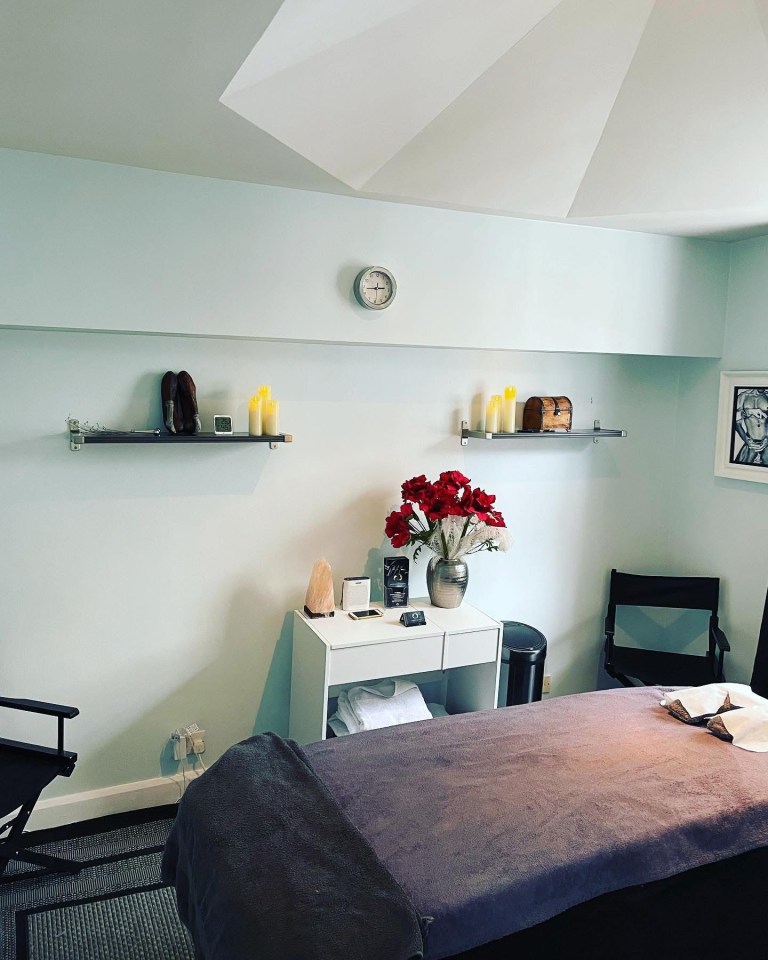 Massage therapy room with a massage table, shelves, and a small desk.