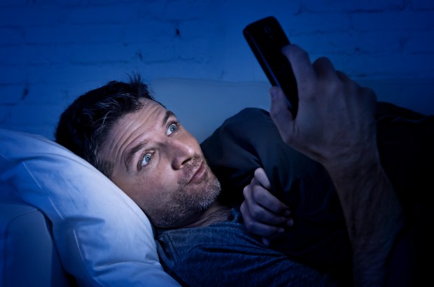 Man lying in bed at night, intently watching his phone.