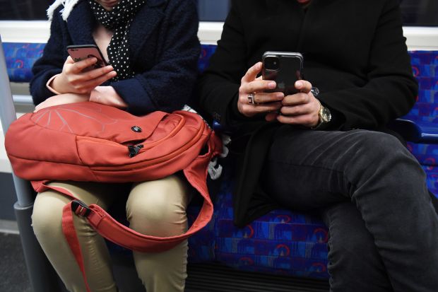 A man and woman using phones on a London Underground train.