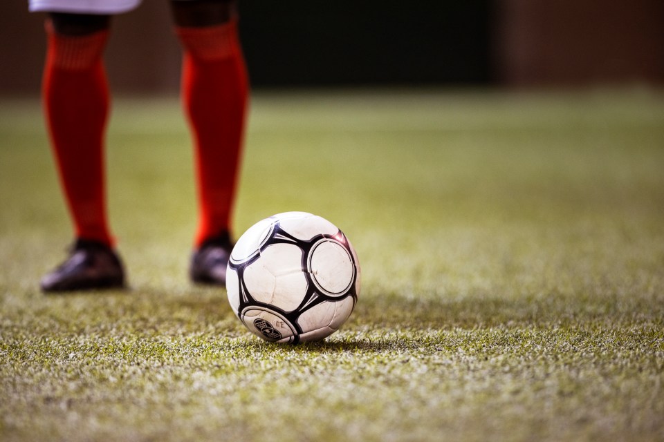 International football player wearing shin guards and cleats positions himself behind a soccer ball on a grass field in big athletic stadium and prepares to kick off professional championship game