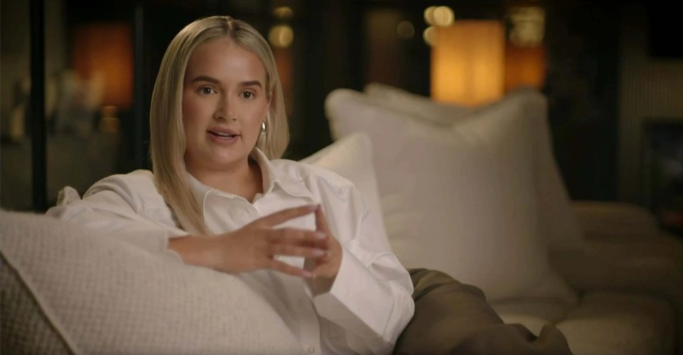 Woman in white shirt speaking on a couch.