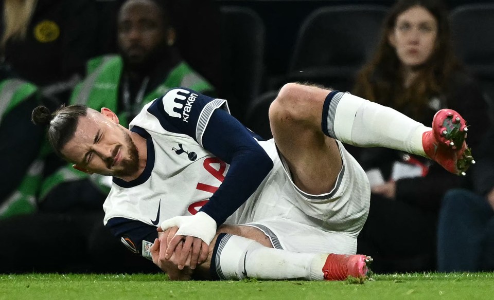 Radu Dragusin of Tottenham Hotspur holding his injured knee on the field.