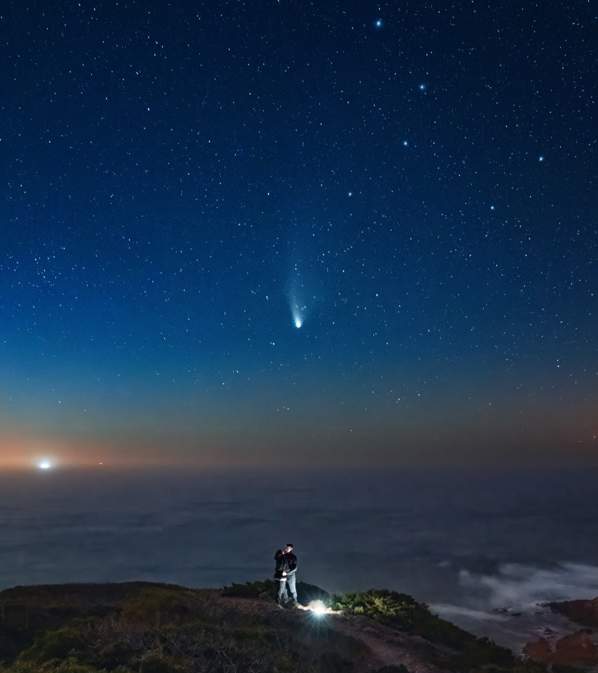 a couple standing on top of a hill under a starry night sky